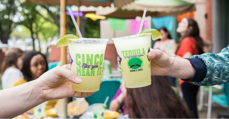 A picture of two hands toasting On The Border margaritas with a bustling street in the background