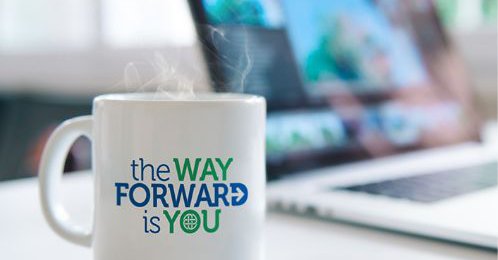 A steaming hot mug sitting on a table with the mug having the text "the WAY FORWARD is YOU"