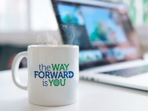 A steaming hot mug sitting on a table with the mug having the text "the WAY FORWARD is YOU"